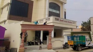 A multi-story building with a large entrance, a sign above the entrance, and a few people and vehicles around. - DWC Residency (Kanchipuram)