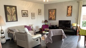 A living room with a sofa, armchair, TV, and artwork on the walls.