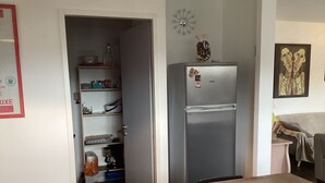 A kitchen with a refrigerator, open pantry, and a table with 'HOT' spelled out on it.
