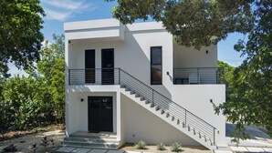 A modern two-story building with a staircase leading to the upper floor, surrounded by greenery. - Take Two! Private Beach House! (Placencia Village)