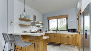 A modern kitchen with a central island, bar stools, wooden cabinets, a microwave, and a refrigerator. - Take Two! Private Beach House! (Placencia Village)