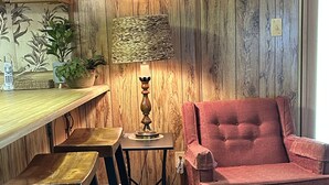 A cozy room with a wooden wall, a bar area with stools, a red chair, and a lamp. - Retro Cottage Farmstay
Mid-term Comfort for Family Relocations/Professionals (Newton)