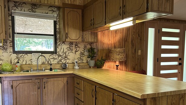 A kitchen with wooden cabinets, a built-in sink, a window with a view, and a hanging lamp. - Retro Cottage Farmstay
Mid-term Comfort for Family Relocations/Professionals (Newton)