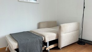 A compact, foldable bed in a room with wooden flooring and a plain white wall. - Centrally located, small apartment with kitchen and shower room 2 (Hamburg)