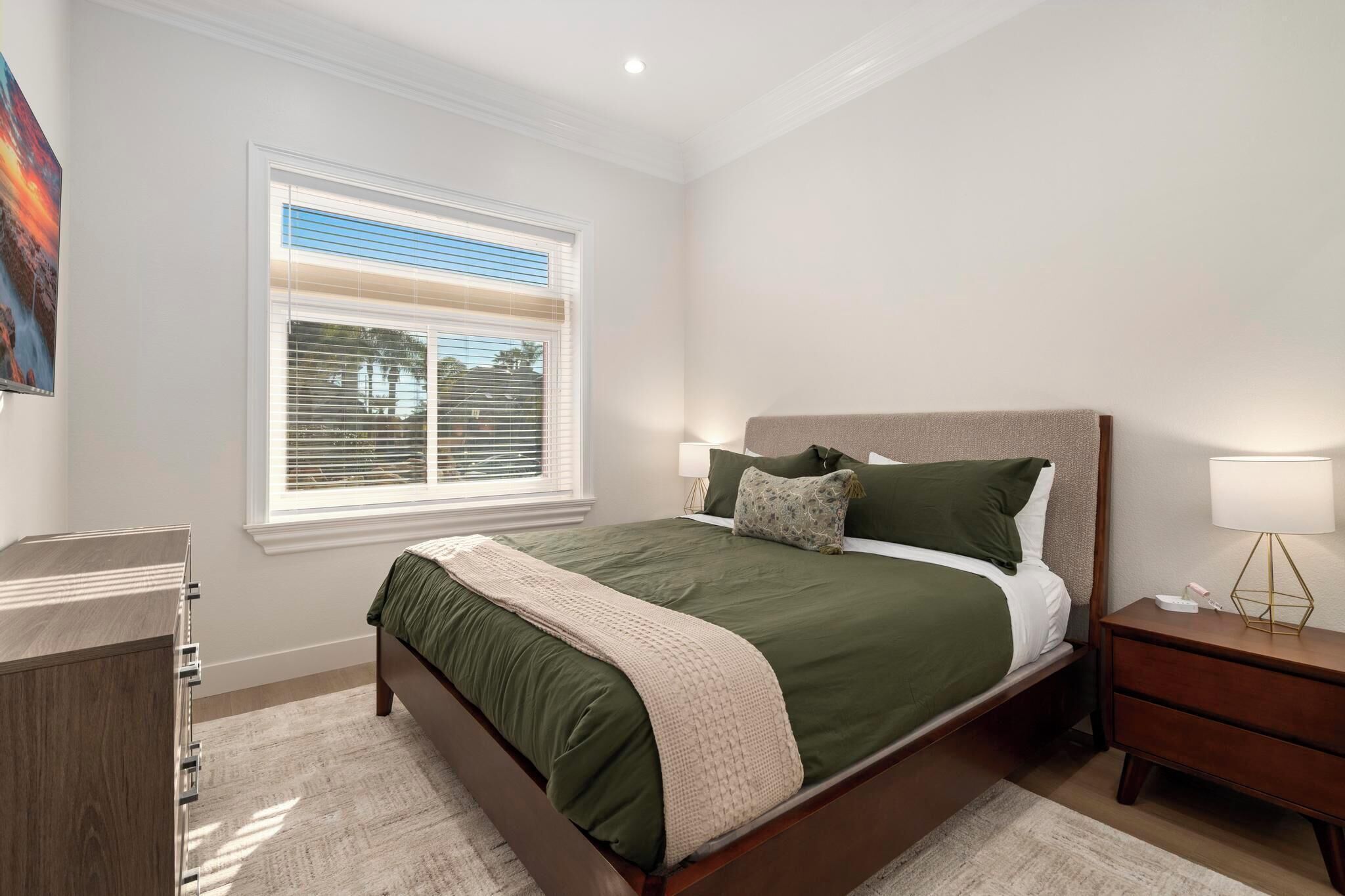A bedroom with a bed, a nightstand, a dresser, and a window with blinds.