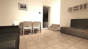 A living room with a sofa, a dining table with chairs, a staircase leading to a balcony, and a framed picture on the wall. - HH Monferrato (Alessandria)