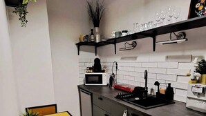 A compact kitchen with a dining table, chairs, a washing machine, and a hanging light fixture. - KK30 Apartment (Budapest)