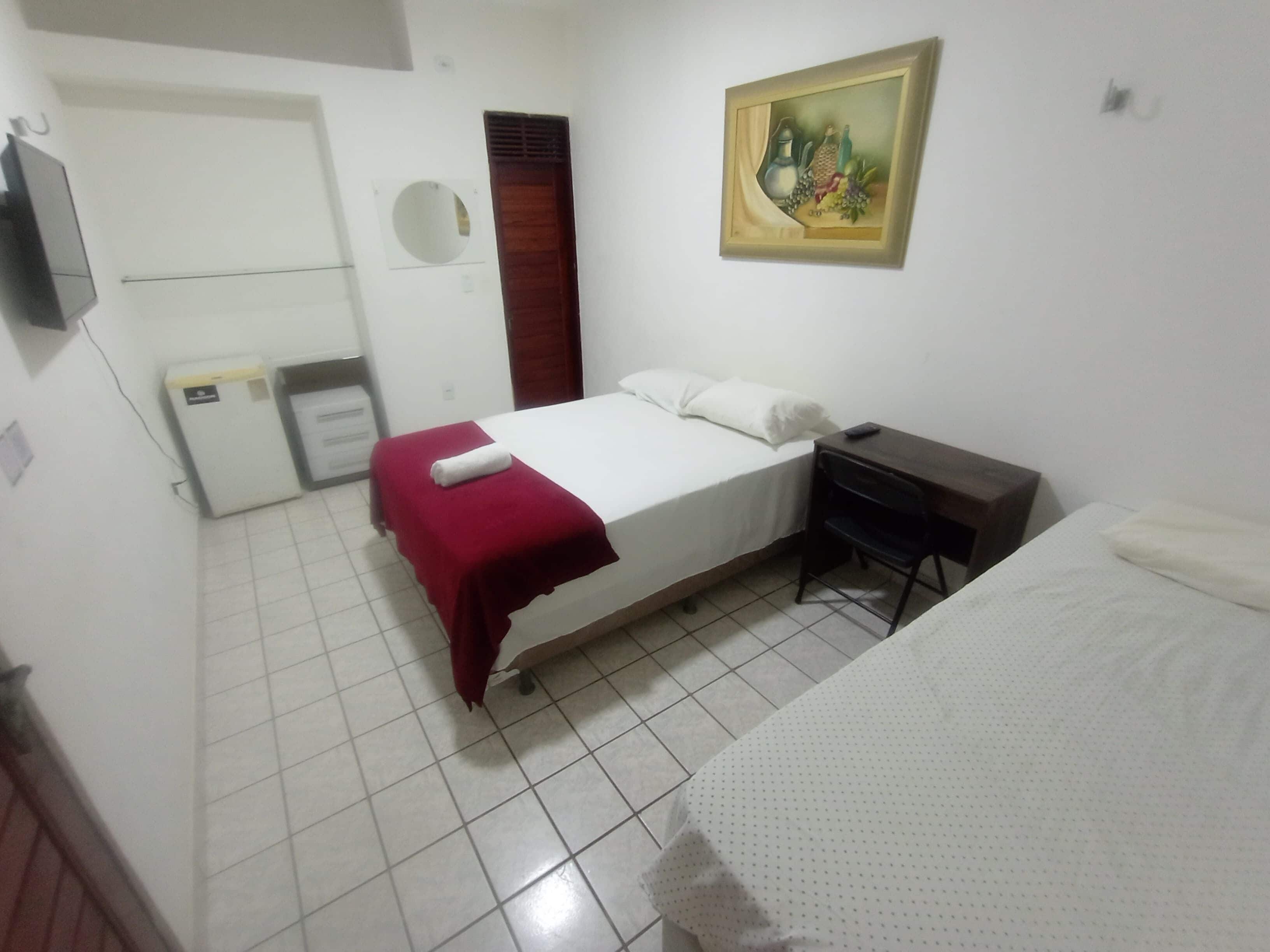 Une chambre à coucher comprenant un lit, un bureau, une chaise, une armoire, un miroir et un tableau accroché au mur.