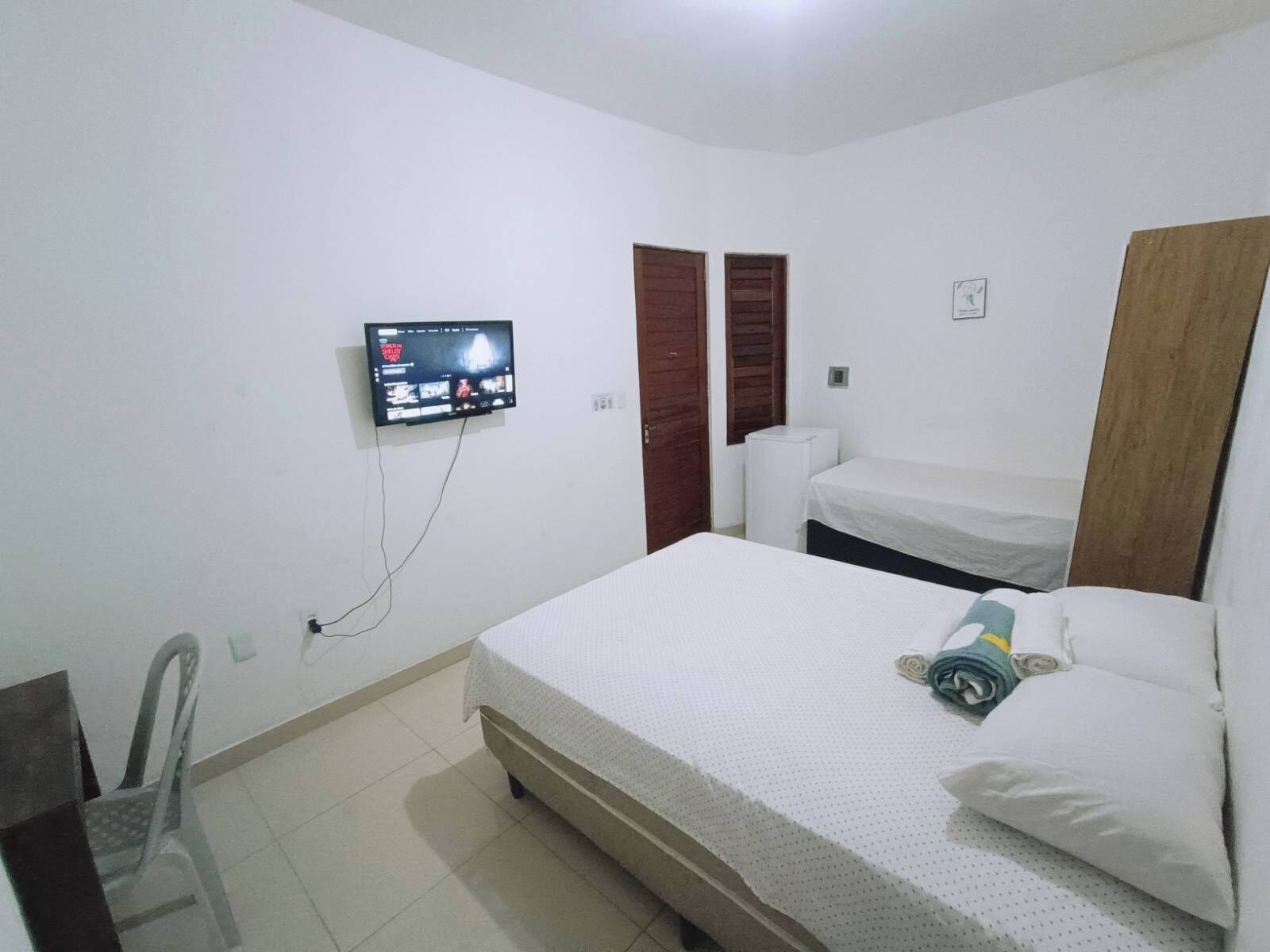 A bedroom with a bed, a TV mounted on the wall, a chair, and a wardrobe.