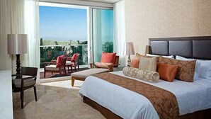 Habitación de hotel con una cama grande, un balcón con sillas y vistas al exterior.