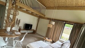 A spacious living area with a high ceiling, a dining table with chairs, a sofa, and a television. - Oak Chalet In Zutendaal (Zutendaal)