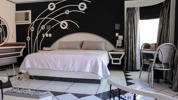 A bedroom with a bed, bedside table, chair, and a decorative wall. - Motel Caribe (Córdoba)