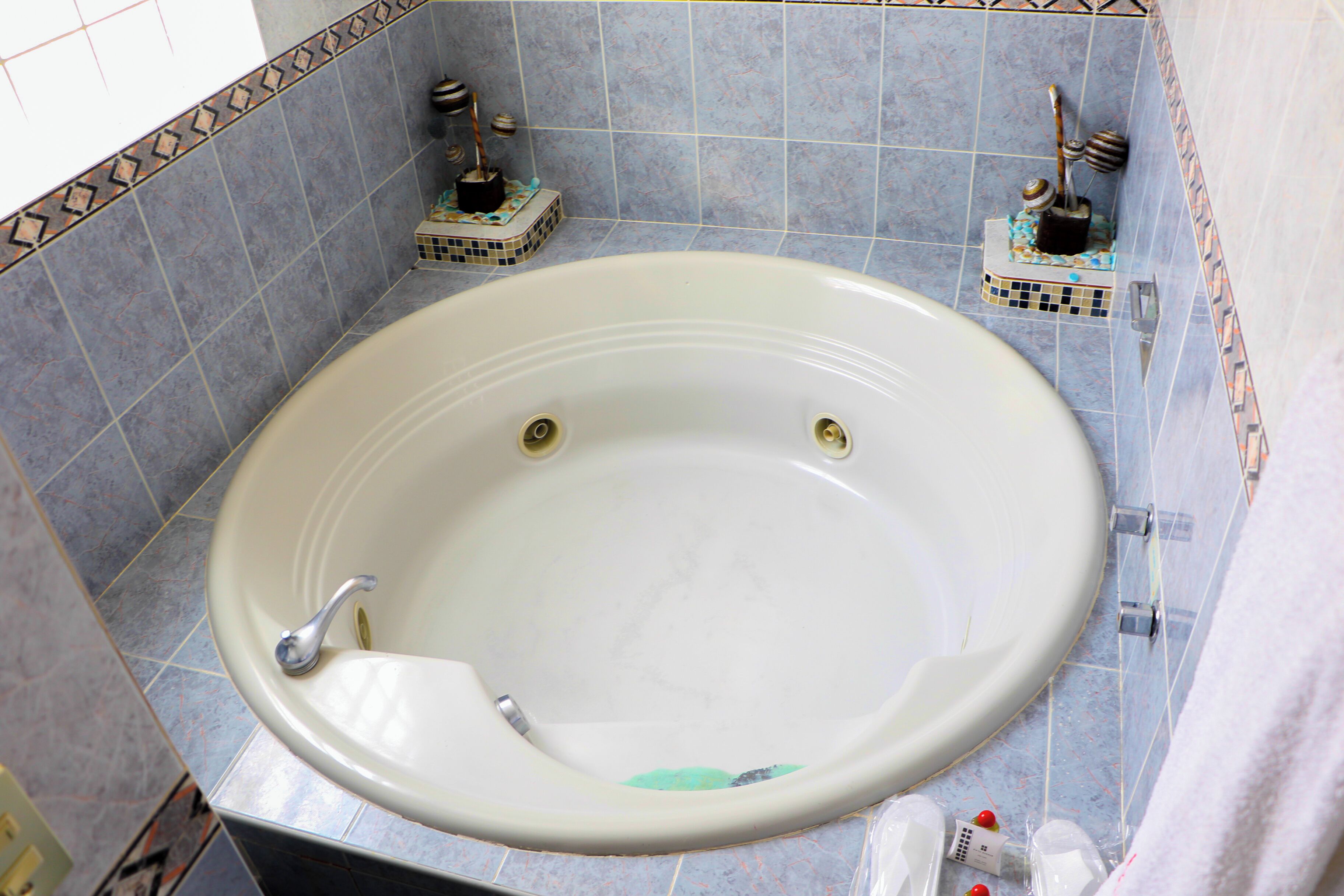 A large bathtub with a faucet, surrounded by blue-tiled walls and a decorative border.