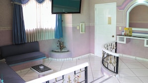 A room with a sofa, a TV mounted on the wall, a small table, and a decorative plant. - Motel Caribe (Córdoba)