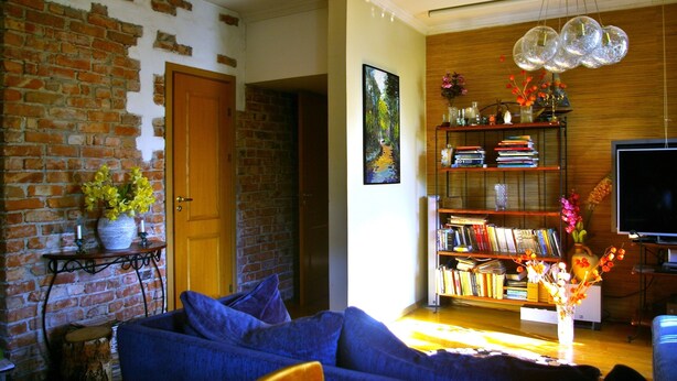 A living room with a brick wall, a wooden bookshelf, a blue sofa, and a television. - Apartment with free parking in central Tallinn (Tallinn)