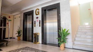 Eine Hotelhalle mit Marmorboden, zwei Aufzügen, einer Rezeption und topfpflanzen.