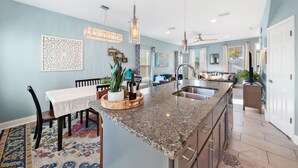 Una cocina moderna con encimeras de granito, un lavaplatos integrado y un comedor con mesa y sillas.