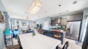 Una cocina moderna con electrodomésticos de acero inoxidable, un comedor con mesa blanca y una sala de estar con sofá y cortinas estampadas.