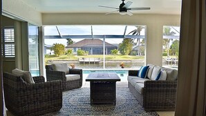 Un patio iluminado por el sol con mobiliario de mimbre, una piscina y vistas a una zona residencial.