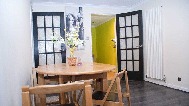 A dining area with a round wooden table, four chairs, and a vase with flowers.