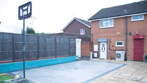 A residential outdoor basketball court with a wooden fence, a brick house, and a red garage door.