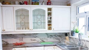 A kitchen with white cabinets, a marble countertop, and a grey tiled floor.