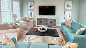 Una sala de estar con un sofá, sillones, una mesa de centro, un televisor y obras de arte en las paredes.