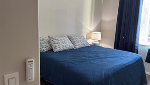 A bedroom with a bed, a nightstand, a lamp, and a window with curtains. - 'Mother-In-Law' apartment in rural neighborhood.King bed, Kitchenette, fullbath. (Wasilla)