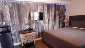 A bedroom with a bed, a TV mounted on a wooden wall, a desk with a chair, and a small refrigerator. - crestwoodmotel (Burlington)