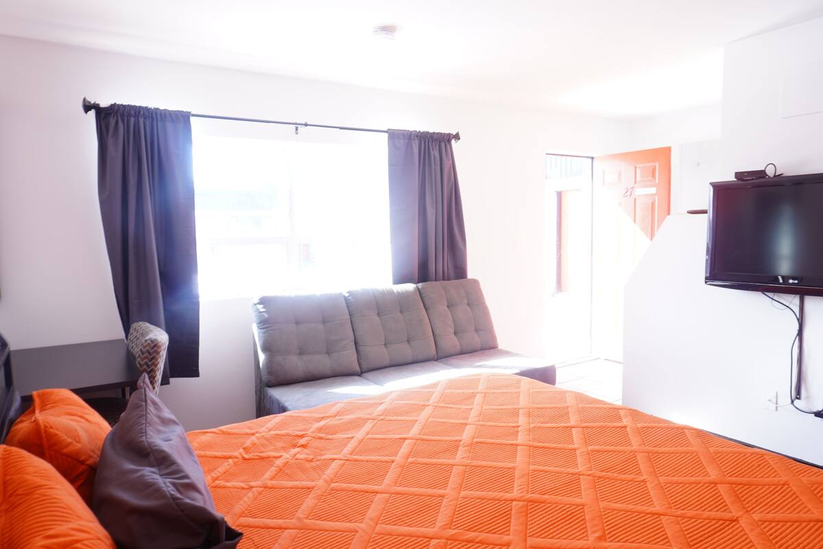 A modern hotel room with a large bed, a flat-screen TV mounted on the wall, and a window with curtains.