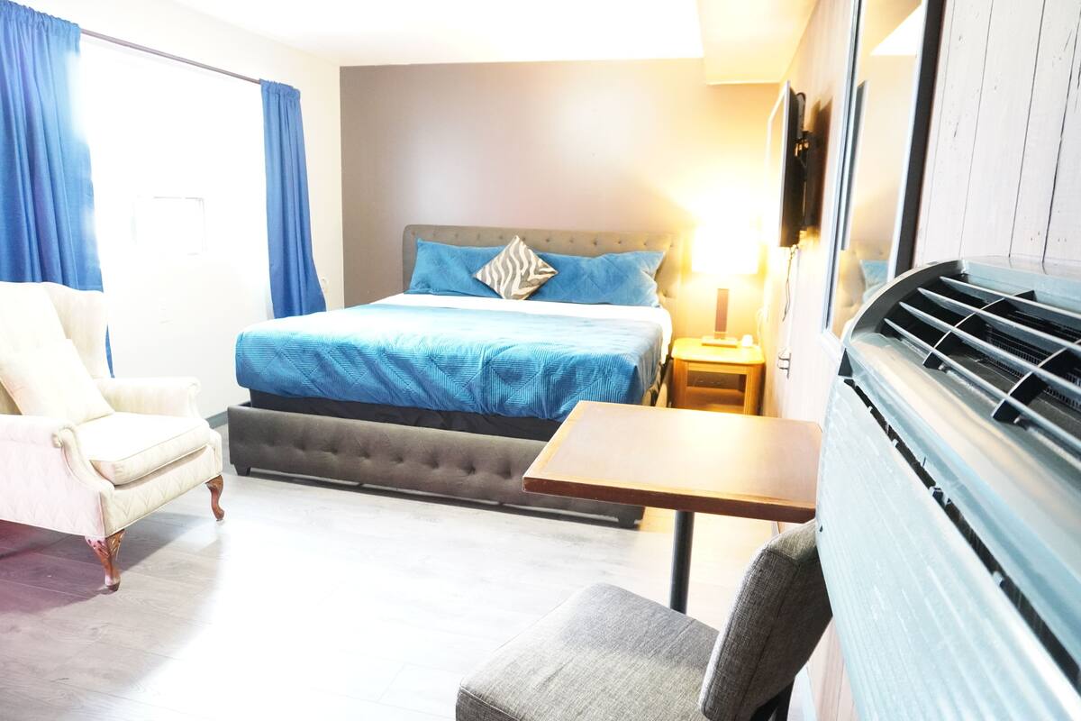 A hotel room with a bed, a chair, a table, and a heater.