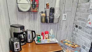 A compact kitchenette with a coffee maker, toaster, kettle, and a tray with food items. - crestwoodmotel (Burlington)