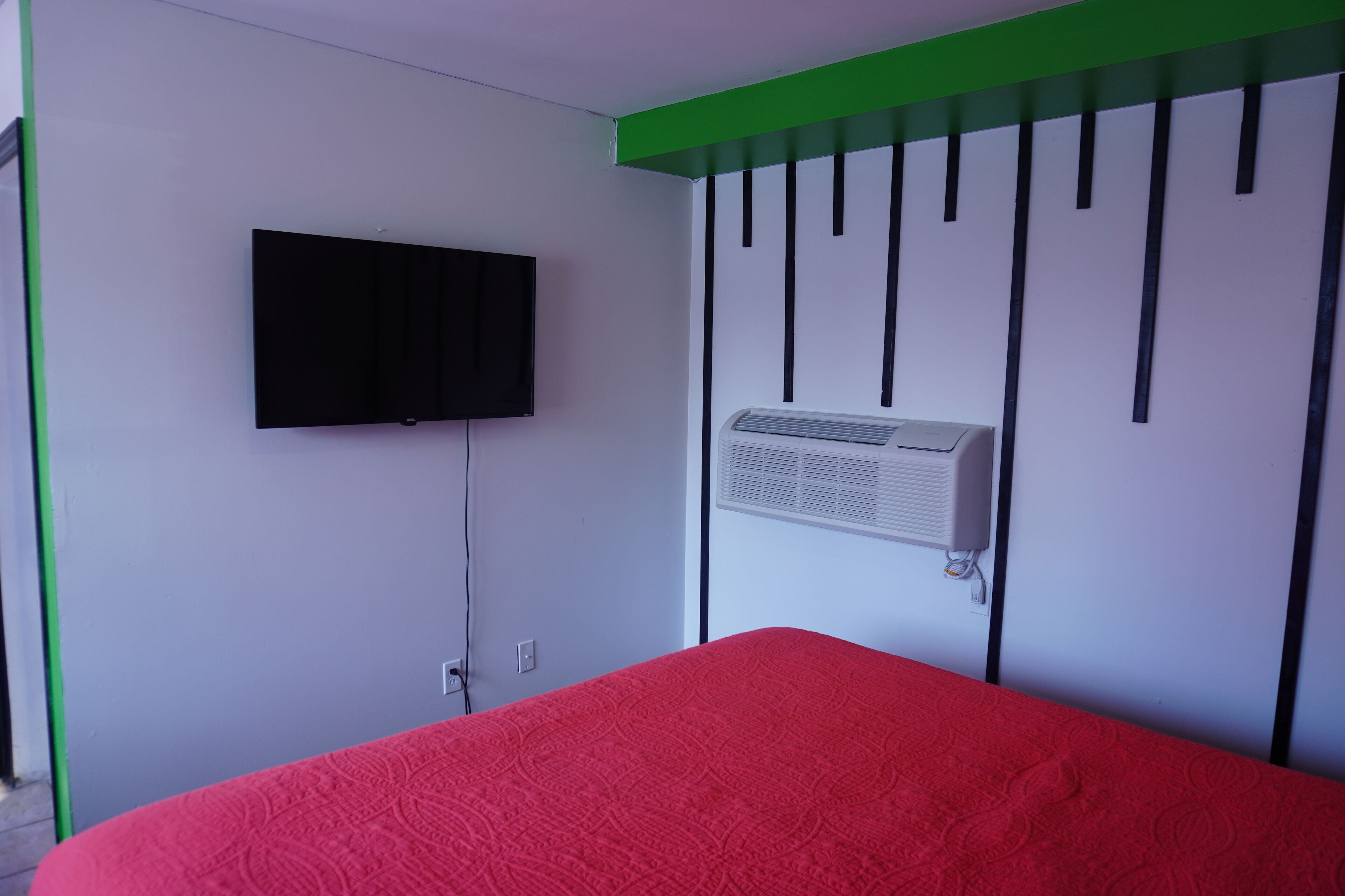Ein Zimmer mit einem Bett, einem an der Wand befestigten Fernseher und einer Wandklimaanlage.
