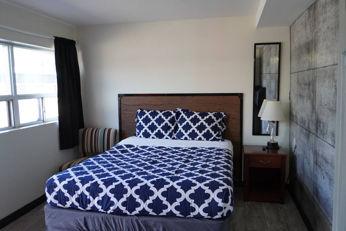 A neatly made bed with a patterned bedspread, a bedside table with a lamp, and a large mirror on the wall.