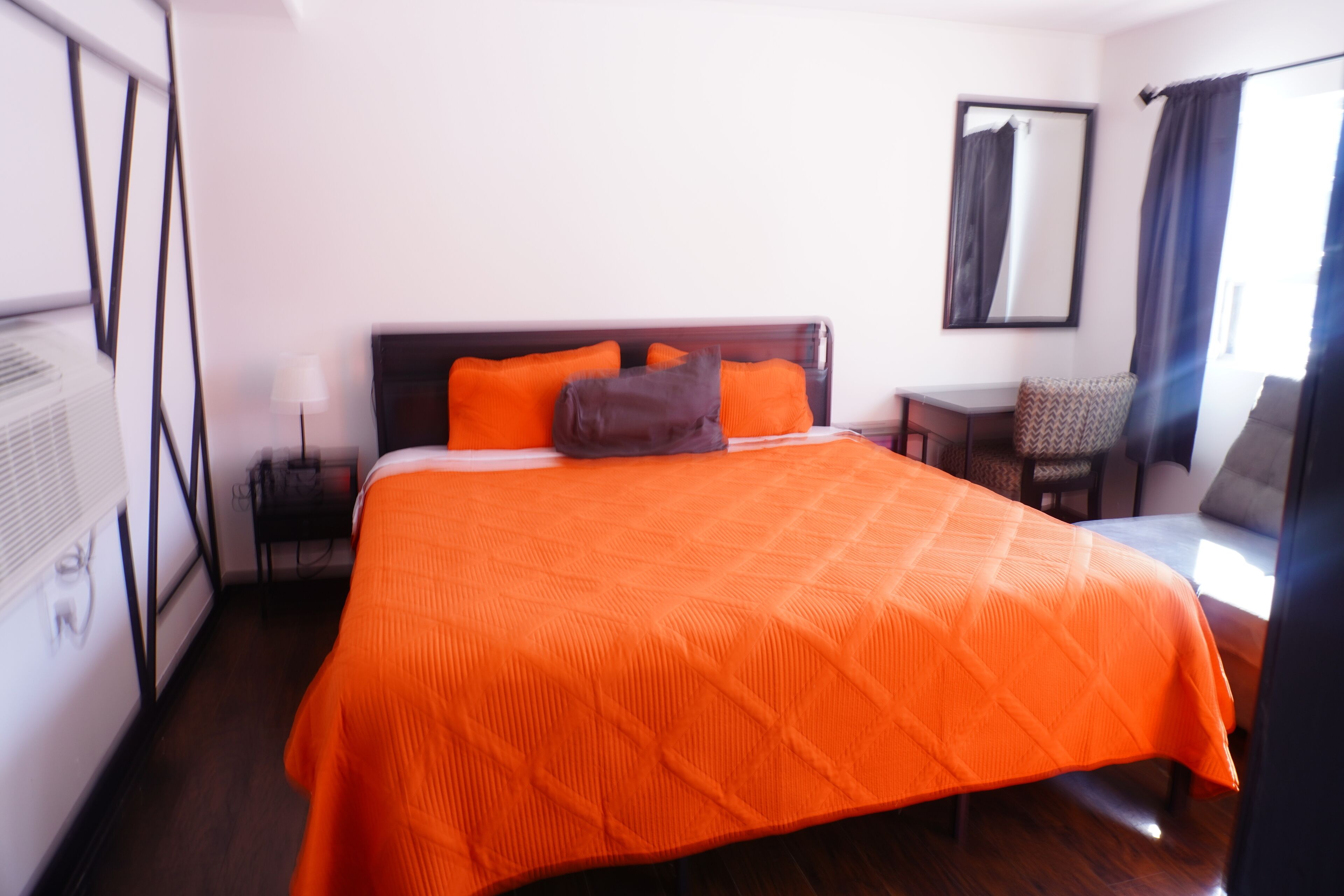 A hotel room with a large bed, an adjacent desk, a chair, and a mirror on the wall.