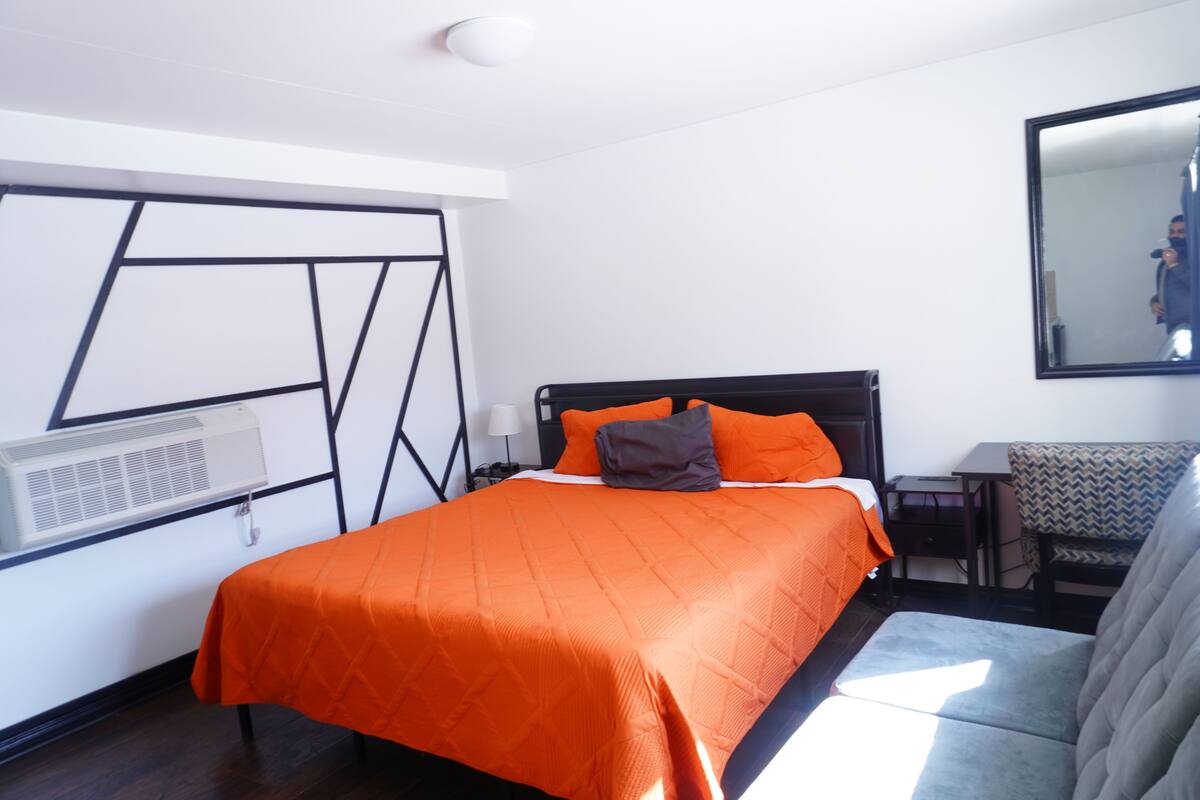 A hotel room with a bed, a desk, a chair, and a large mirror.