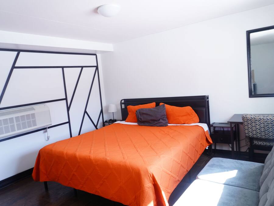 A hotel room with a bed, a desk, a chair, and a large mirror.