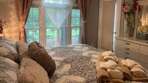 Ein Schlafzimmer mit einem großen Bett, einem Baldachin, einem Schminktisch mit Spiegel und einem Fenster mit Vorhängen.
