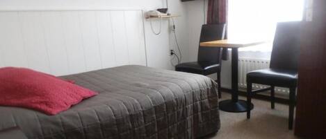 Un dormitorio con cama, escritorio, dos sillas, televisor y radiador.