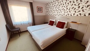 Une chambre d’hôtel avec deux lits, un bureau, une chaise et un radiateur.