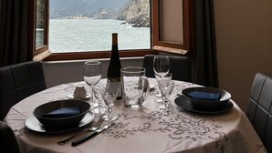 A table set for two with a bottle of wine, glasses, and plates, overlooking a coastal view with mountains.