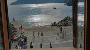A view from a window overlooking a beach with people walking and sitting, and boats on the water.