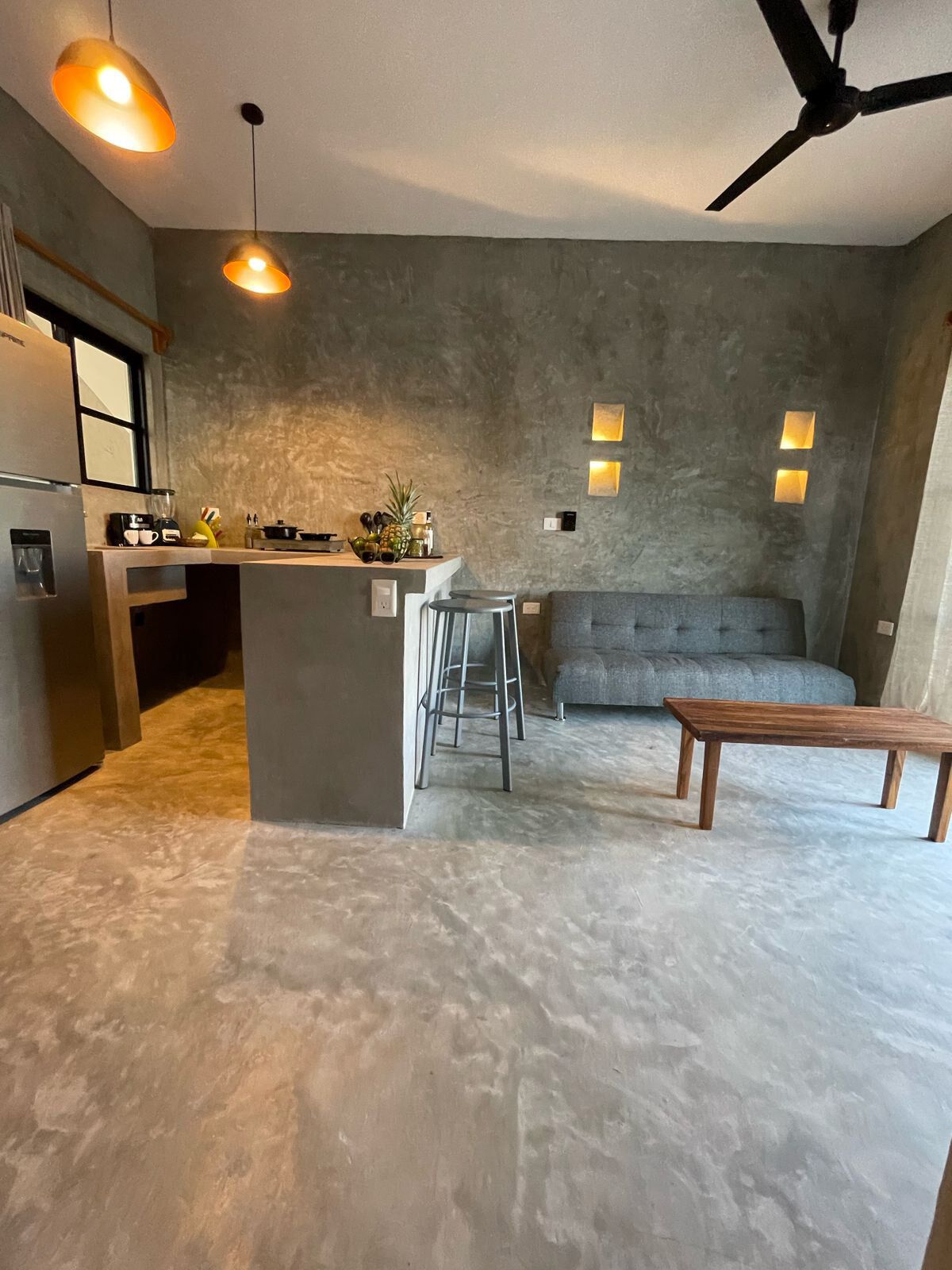 Una cocina moderna con una isla central, taburetes de bar, un sofá gris y una mesa de madera.