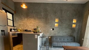 Eine moderne Küche mit einer zentralen Kochinsel, Barhocker, einem grauen Sofa und einem Holztisch.