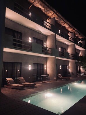 Un hotel de varios pisos con piscina, zona de estar al aire libre y techo de paja.