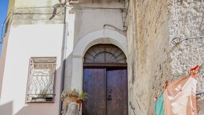 A set of stone steps leading to a wooden door with a metal gate, flanked by a wall with a small window and a potted plant.