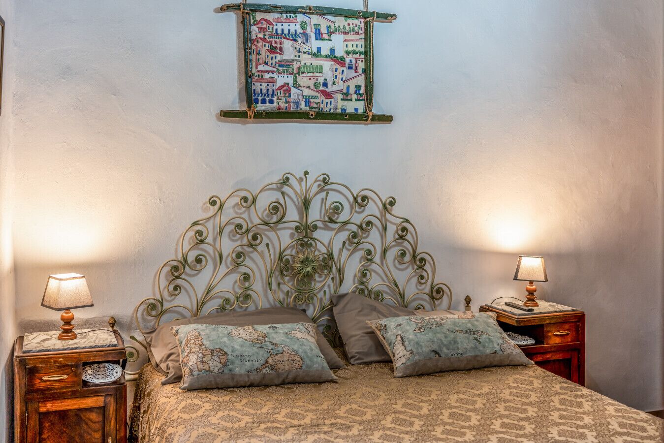 Une chambre à coucher avec une tête de lit en métal, deux tables de chevet avec des lampes, un lit avec une literie à motifs et une œuvre d’art représentant une carte du monde accrochée au mur.