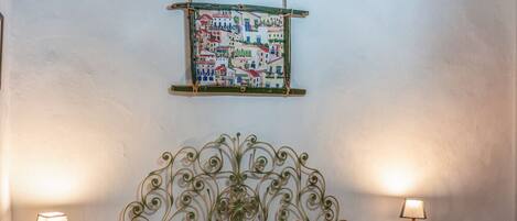 Une chambre à coucher avec une tête de lit en métal, deux tables de chevet avec des lampes, un lit avec une literie à motifs et une œuvre d’art représentant une carte du monde accrochée au mur.