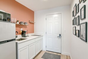 Una cocina con armarios blancos, un refrigerador blanco, una cafetera y un microondas.