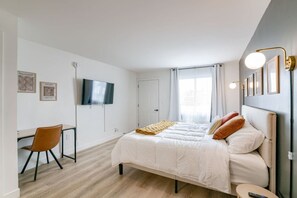 Un dormitori amb llit, escriptori, cadira, televisió i finestra amb cortines.